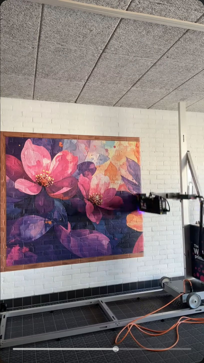 Veliki cvjetni mural u ružičastim i ljubičastim tonovima na bijelom ciglenom zidu fitness studija.